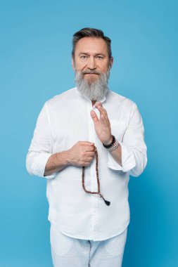 Gri saçlı usta guru tespih ile mavi üzerine izole edilmiş kutsama hareketi gösteriyor.