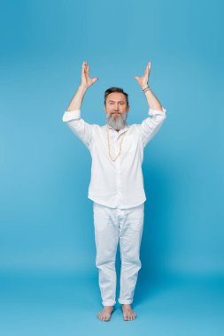 Yoga ustasının tam boy meditasyonu. Kaldırılmış ellerle, mavinin üzerinde beyaz duruyor. 