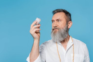 Gri sakallı dahi guru mavi üzerinde izole edilmiş selenit kristaline bakıyor.