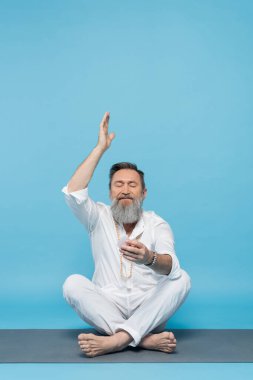 Beyaz elbiseli son sınıf öğrencisi, kristal kristalle meditasyon yapıyor. Mavi ellerle poz veriyor.