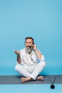 yoga koçu, kulaklıkla yoga minderinde rahat poz veriyor ve elini maviye doğrultuyor. 