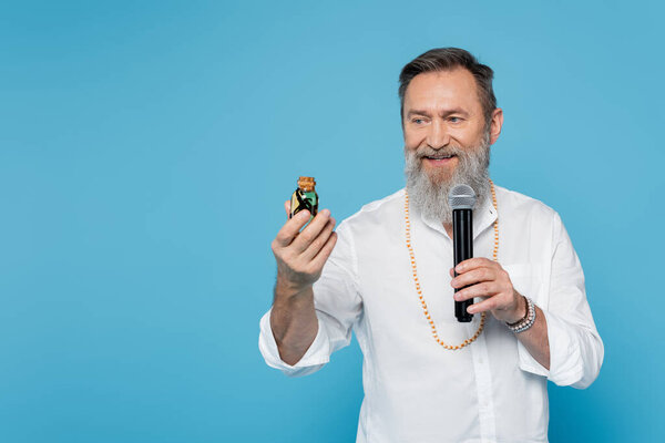 smiling ayurveda guru with bottle of essential oil talking in microphone isolated on blue