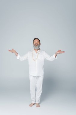 Gülümseyen yoga gurusu, ağaçta meditasyon yapıyor, kollarını griye açmış.