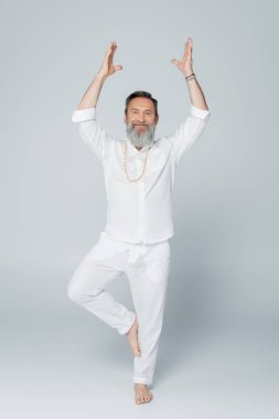 Yaşlı yoga koçunun ağaçta meditasyon yapması ve gri ellerle durması.