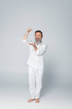 Yoga hocasının tam uzunluğunda, sallanan sarkacıyla gri kameraya bakıyor.