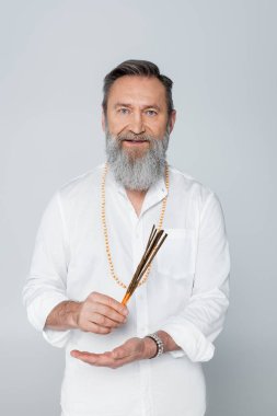 Aroma çubuklarıyla ayurveda ustası Gri üzerine izole edilmiş kameraya bakıyor