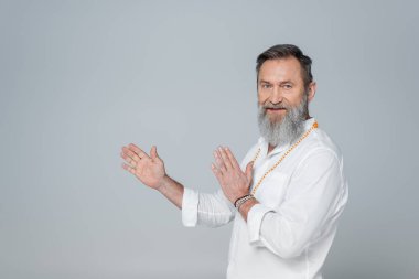 Ruhani guru kameraya bakıyor ve gri üzerine izole edilmiş ellerle işaret ediyor