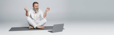 Üst düzey yoga koçu, çene Mudra 'yı dizüstü bilgisayarın yanında gri pankartta otururken gösteriyor.