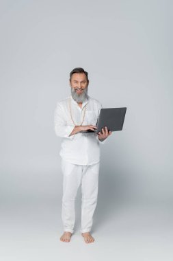 Tam boy sakallı yoga koçu dizüstü bilgisayarını griye takmış duruyor.