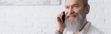 Gülümseyen sakallı manevi akıl hocası evde cep telefonuyla konuşuyor.
