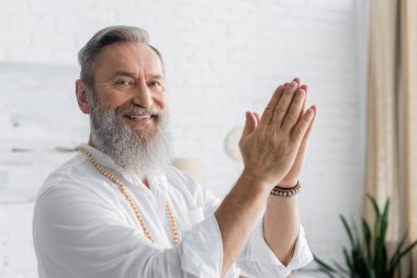 Sakallı ruhani koç kameraya gülümsüyor ve Anjali Mudra 'yı gösteriyor