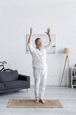 full length of senior man in white clothes meditating in crescent moon pose with raised hands clipart