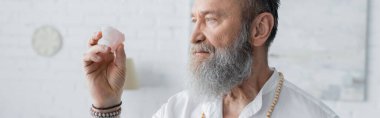 Sakallı guru adam evde meditasyon yaparken selenit kristale bakıyor.