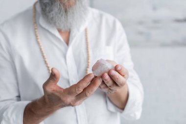 cropped view of master guru holding spiritual selenite stone on blurred background clipart
