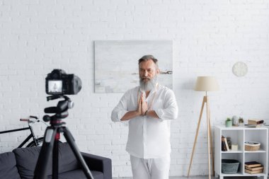 Sakallı usta guru evde dijital kameranın önünde dua eden ellerle meditasyon yapıyor.