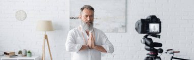Sakallı guru adam, dijital kameranın yanında dua eden ellerle meditasyon yapıyor.