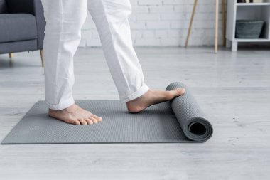 Çıplak ayaklı adamın evde yoga minderini açarken kısmi görüntüsü