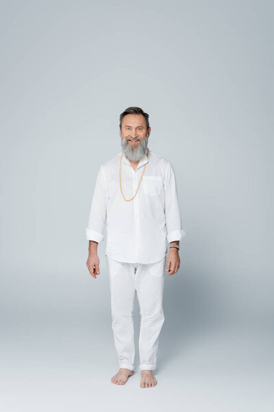 на всю длину улыбающегося босоногого гуру в белой одежде стоящего на сером