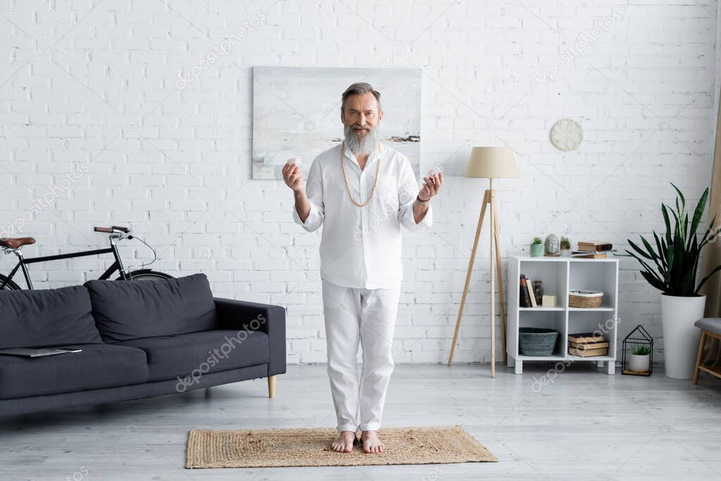 full length of yoga guru in white clothes standing with selenite stones at home