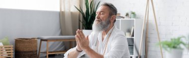 Usta guru kapalı gözlerle meditasyon yapıyor ve evde dua eden eller, bayrak