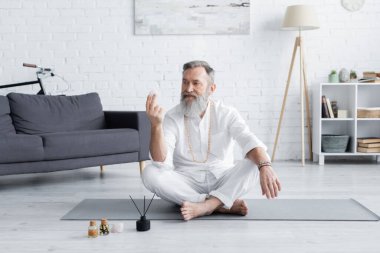 Kokulu yağ ve aroma çubuklarının yanında selenit taşıyla oturan yoga gurusu.