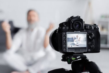 Yaşlı yoga koçunun yanındaki dijital kameranın seçici odağı kolay bir şekilde meditasyon yapıyor.