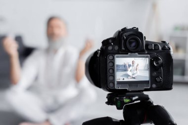 selective focus of digital camera near senior yoga coach meditating in easy pose clipart