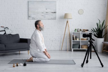 Yoga ustasının gök gürültüsü üzerinde meditasyon yaparken yan görüntüsü kokulu yağlar ve dijital kameranın yanında duruş