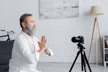 Beyin gurusu kapalı gözlerle meditasyon yapıyor ve dijital kameranın yanında dua eden eller.