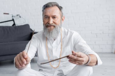 Beyaz gömlekli ve boncuklu usta guru evde aroma çubuğu tutuyor.