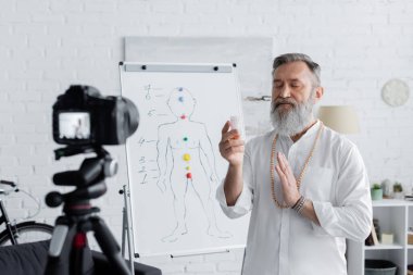 ruhani guru, dijital kameranın yanında selenit taşla meditasyon yapıyor ve insan çakraları şeması ile çevirme çizelgesi yapıyor.