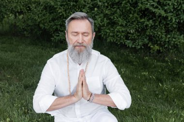 Usta guru kapalı gözlerle meditasyon yapıyor ve bahçede dua eden eller.