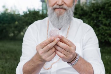 Sakallı ruhani akıl hocasının boncuklu bilezikleri içinde açık havada selenit taşıyla meditasyon yaparken kısmi görüntüsü.