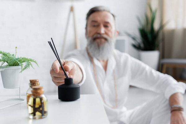 selective focus of essential oils and diffuser with aroma sticks near blurred healing guru