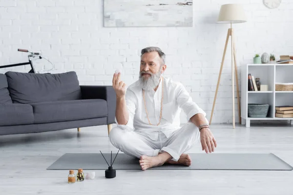 senior yoga guru sitting with selenite stone near scented oils and aroma sticks