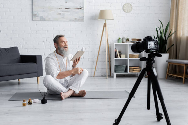 yoga master reading manual while sitting in easy pose near essential oils and digital camera