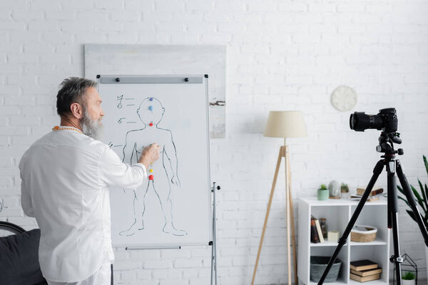 ayurveda guru near flip chart with human chakras system and digital camera