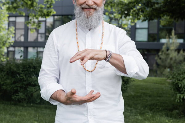 cropped view of bearded man in white shirt showing energy gesture outdoors