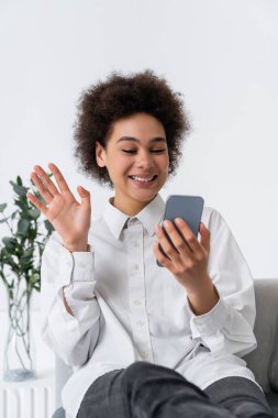 Neşeli Afrikalı Amerikalı kadın akıllı telefondan video görüşmesi sırasında el sallıyor. 