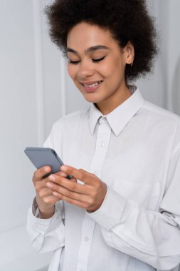 Neşeli Afrikalı Amerikalı kadın evde akıllı telefondan mesajlaşıyor. 