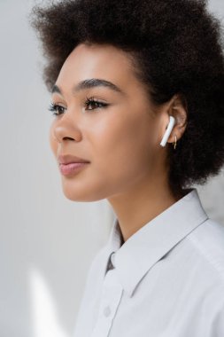 portrait of curly african american woman listening music in wireless earphone clipart