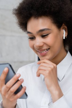 Mutlu Afro-Amerikan kadınlarına yakın çekim kablosuz kulaklıkla müzik dinleyen ve akıllı telefon kullanan
