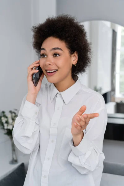 アフリカ系アメリカ人女性が携帯電話で話し現代のリビングルームでジェスチャーをし — ストック写真