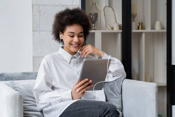 happy african american woman in wired earphones holding digital tablet while watching comedy movie