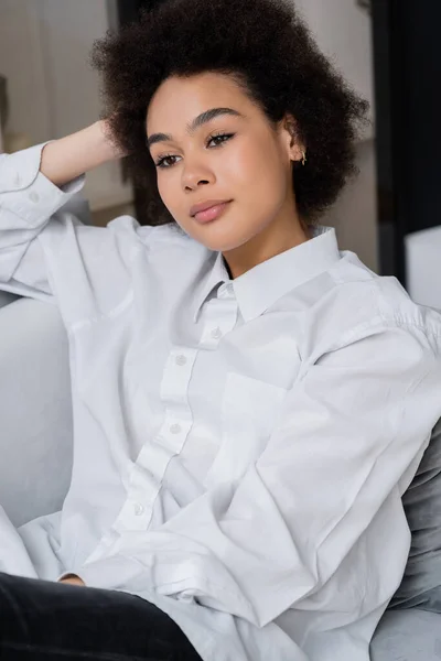夢のようなアフリカ系アメリカ人女性の白いシャツにグレーのアームチェアに座っている襟付きの肖像画 — ストック写真