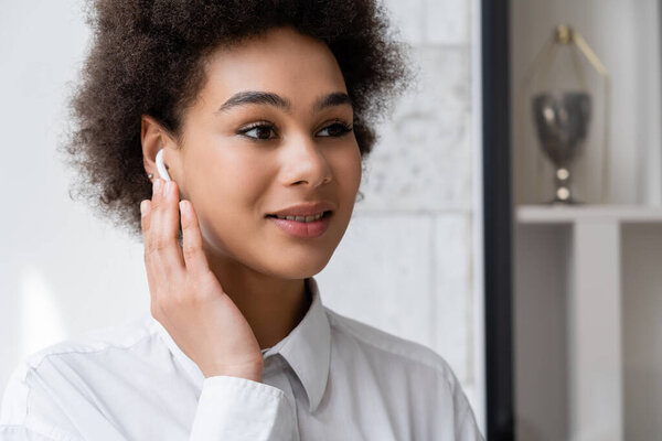 portrait of happy african american woman listening music and adjusting wireless earphone 