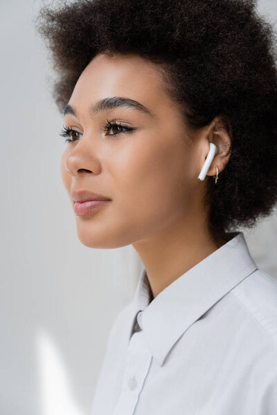 portrait of curly african american woman listening music in wireless earphone