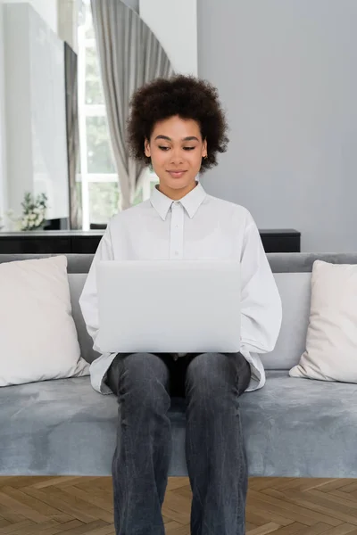 Leende Afrikansk Amerikansk Kvinna Använder Laptop Medan Sitter Grå Sammet — Stockfoto