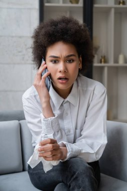 Beyaz gömlekli Afro-Amerikan kadın akıllı telefondan konuşuyor. 