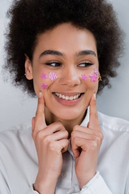Afro-Amerikan kadın portresi dekoratif mor yıldızlarla parmaklarıyla yanakları gösteriyor.